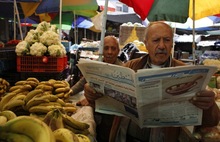 A Palestinian man selling fruits and vegetables reads a copy of a pro-Hamas newspaper, Palestine, at a market in the West Bank city of Ramallah